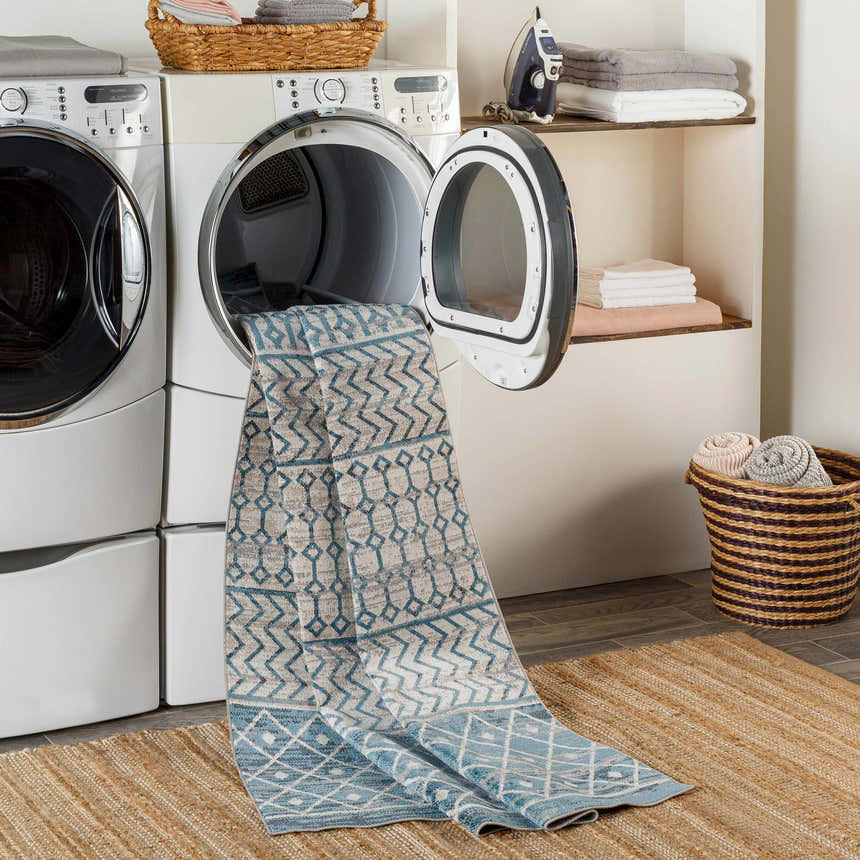 Laundry room scene with Pinamopoan Washable Area Rug in blue and gray coming out of the dryer. Jute rug underneath. Washing-Machine