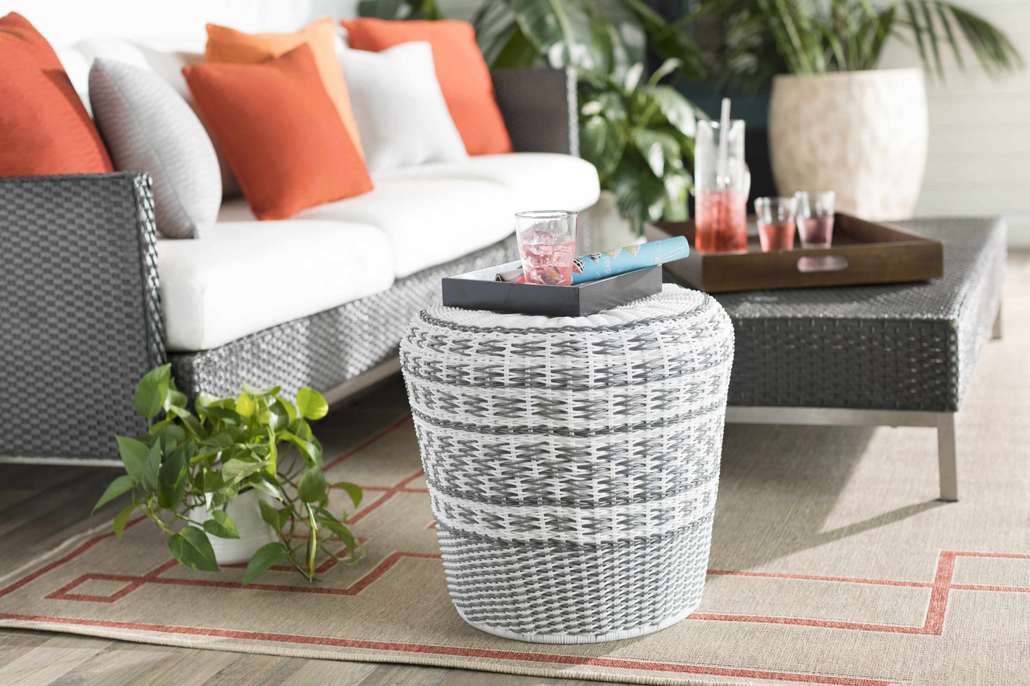 Patio scene with brick red Moffett Area Rug, gray wicker furniture, and orange pillows for a cozy outdoor living space. Styleshot