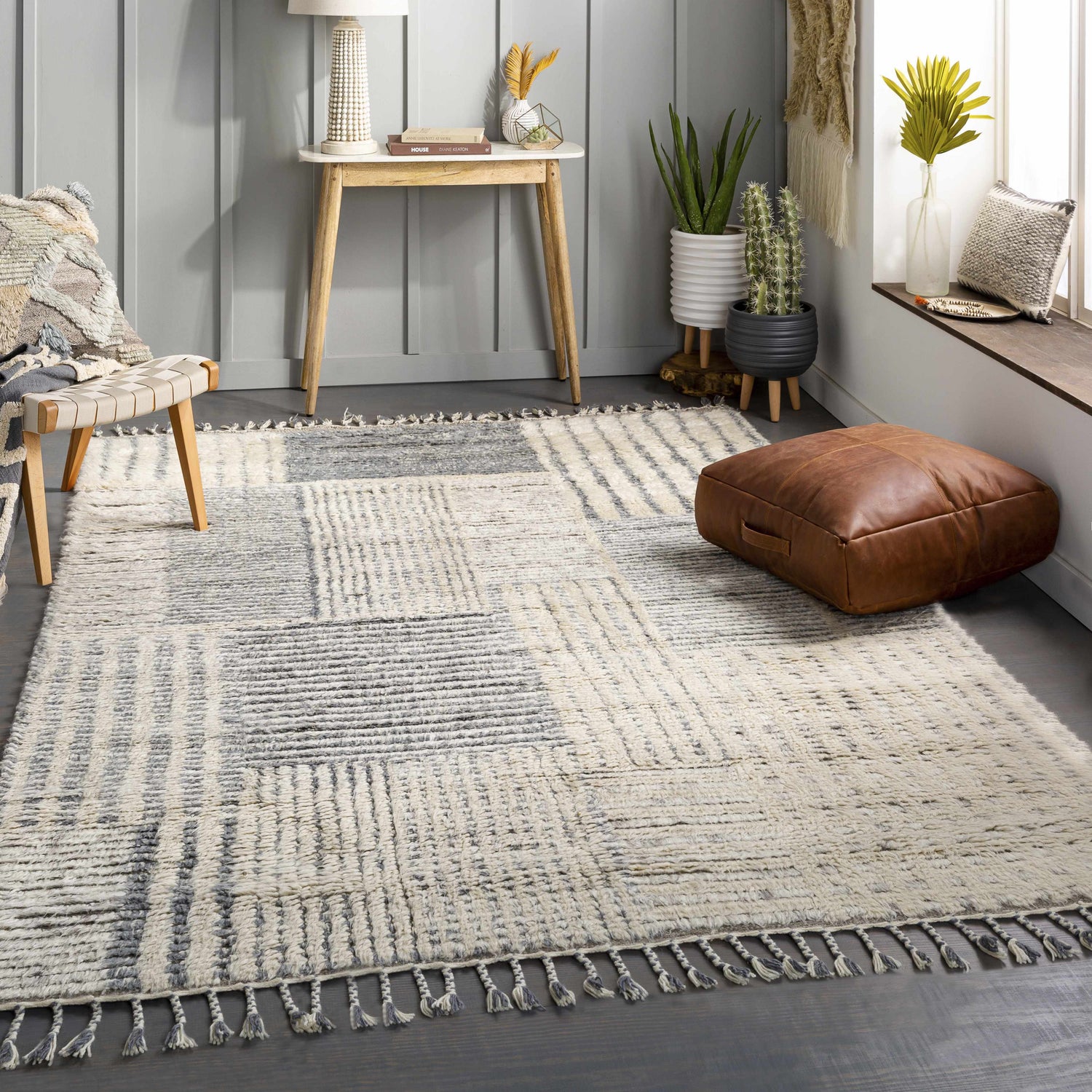 Living room scene with a cream and charcoal Plean Premium Rug, wood stool, and leather ottoman. Roomscene-Rectangle