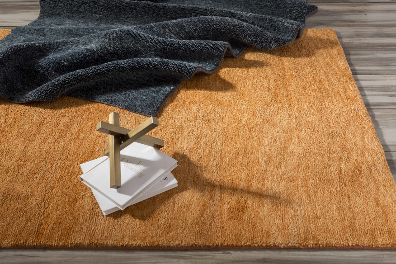 Close-up of the textured, burnt orange Plainville Area Rug. Gray throw blanket and decor books are styled on the wool rug. Styleshot