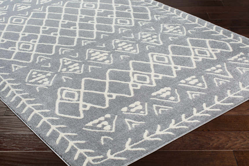 Close-up of the Plumsteadville Area Rug in cream and slate, featuring a geometric farmhouse pattern on dark wood floors. Corner