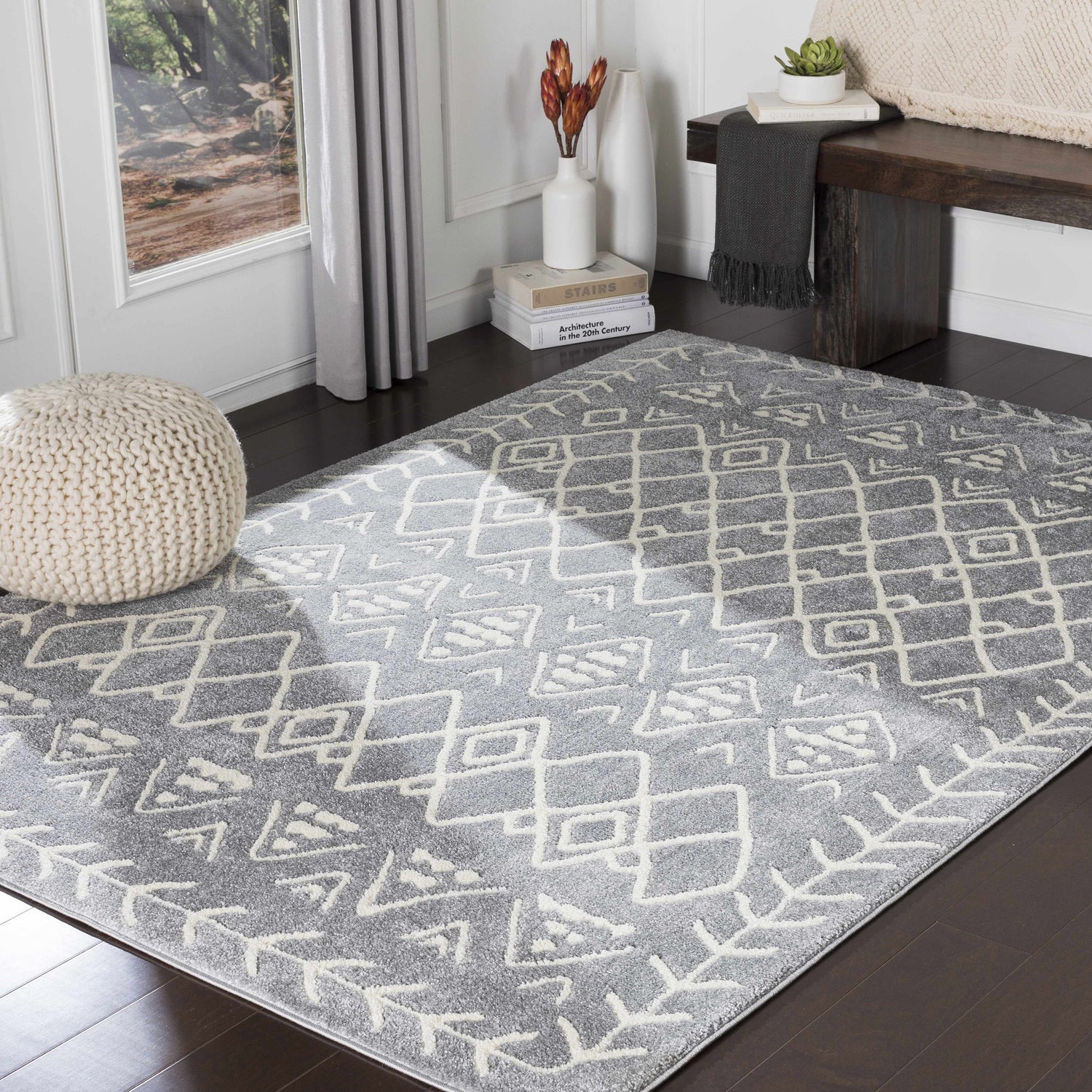 Living room scene with slate and cream Plumsteadville Area Rug, wood bench, and knit pouf. Roomscene-Rectangle