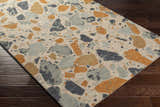 Close-up of the Panabingan Area Rug showing brick red, dark blue, beige, and sage shapes on a textured wool rug. Corner