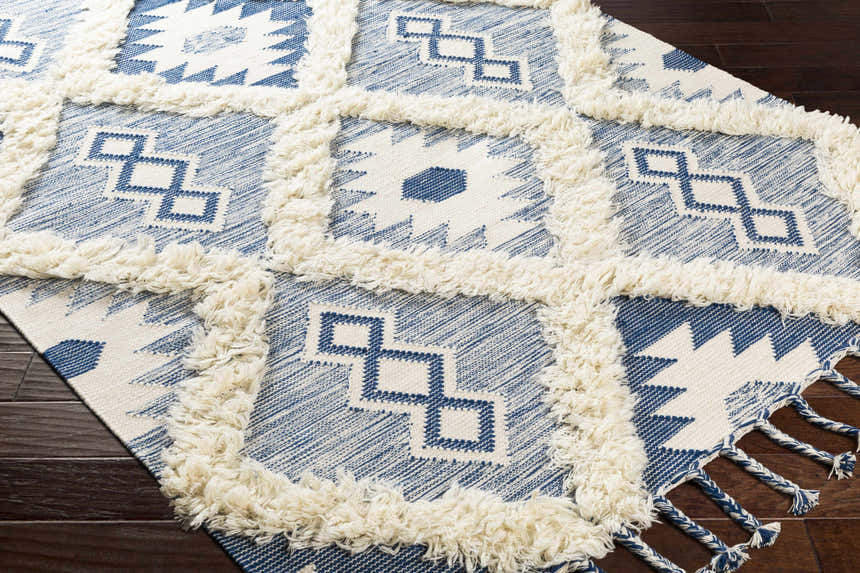 Close-up of Painesdale Blue/White Wool Carpet with geometric pattern, ivory fringe, and blue tassels. Corner