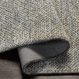 Close-up of the hand-loomed Pantubig Area Rug. Charcoal, gray, ivory, and beige textured wool and viscose rug on wood floor. Fold