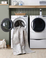 Laundry room scene with PNW Home Rainier Damask Light Brown Washable Rug draped from a washing machine. Farmhouse style. Washing-Machine