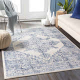 Living room scene with a blue and off-white Pooraka Area Rug, sofa, chair, and pouf. Roomscene-Rectangle