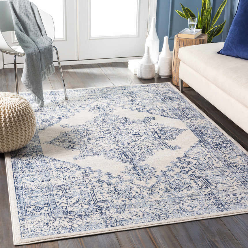 Living room scene with a blue and off-white Pooraka Area Rug, sofa, chair, and pouf. Roomscene-Rectangle