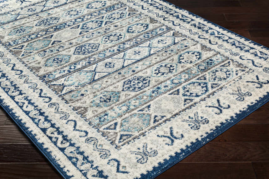 Close-up of the Purdys Area Rug featuring a Bohemian-style pattern in aqua, charcoal, and cream on a dark wood floor. Corner