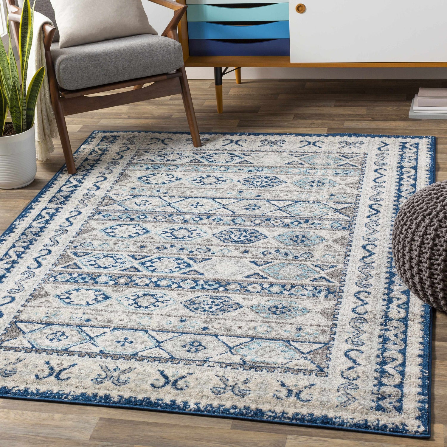 Living room scene with a Bohemian style Purdys Area Rug in aqua, charcoal, and cream colors, wooden chair, and mid-century modern cabinet. Roomscene-Rectangle