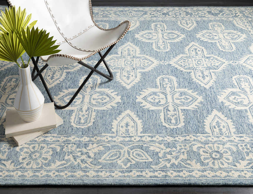 Coastal living room scene with a blue and light beige Passaic Hand Tufted Wool Rug. White chair and palm leaves add to the decor. Styleshot