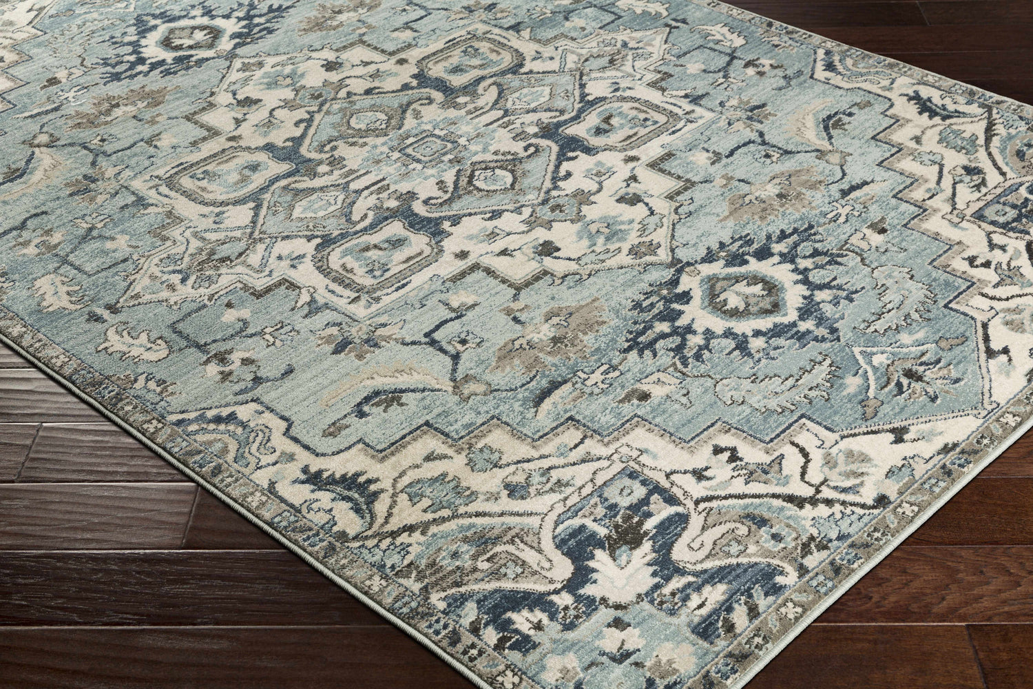 Close-up of the Pukwana Area Rug. Machine-woven rug with a traditional design in shades of blue, gray, and oatmeal. Corner