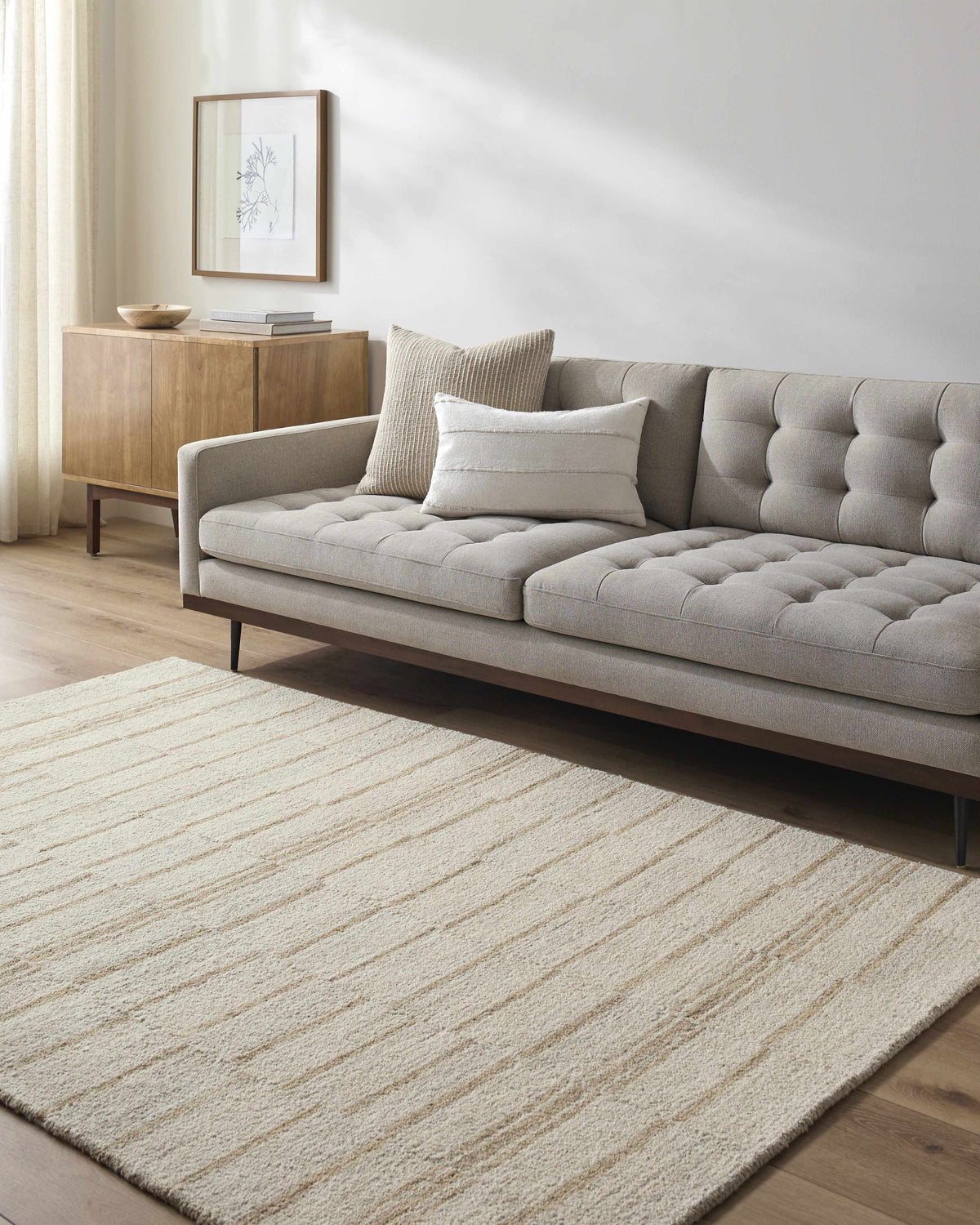 Living room with a beige Abbatha Modern Wool Rug, gray sofa, and wood cabinet. Roomscene-Rectangle