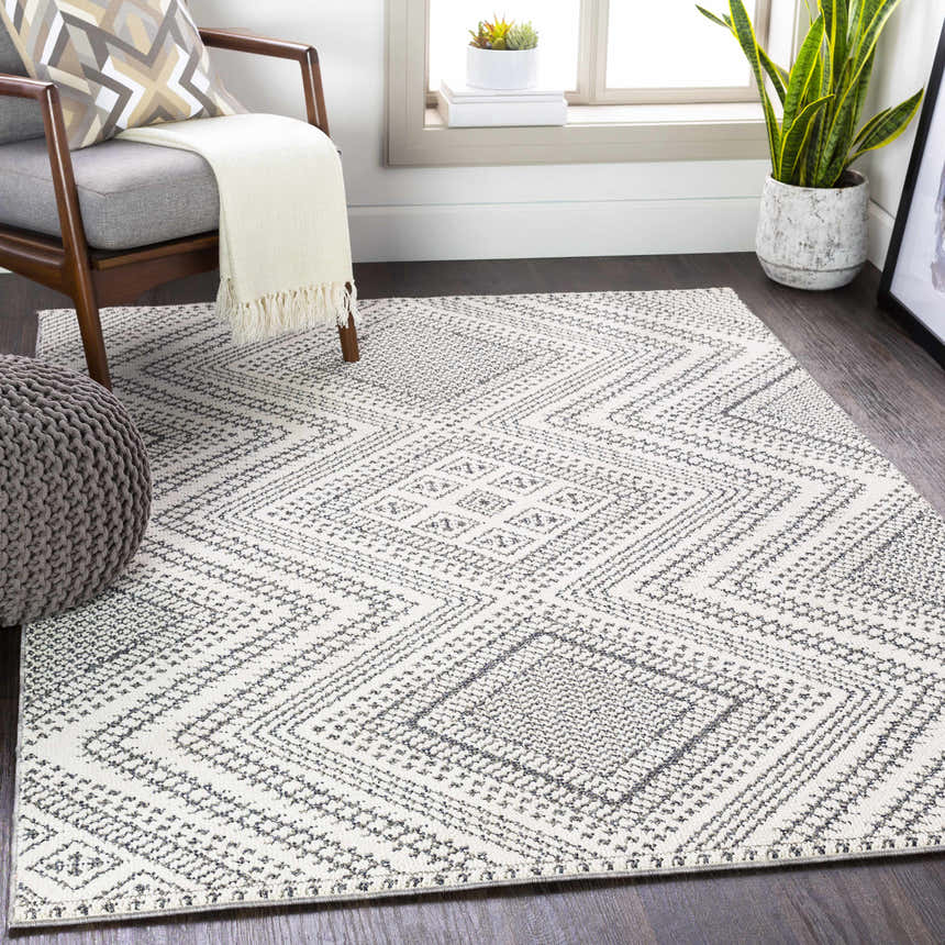 Living room scene with a gray chair and the geometric black and white Queanbeyan Area Rug. Roomscene-Rectangle