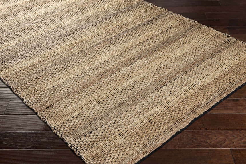 Close-up of the hand woven Quebradillas Area Rug. Jute rug with black and light olive stripes on dark wood floor. Corner