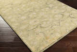 Close-up of the Raceland Area Carpet. Hand-knotted wool rug in beige, light olive, and mustard on dark wood flooring. Corner