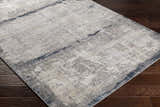 Close-up of Rainworth Modern Slate Luxe Rug showing charcoal, beige, and gray abstract pattern on dark wood floor. Corner