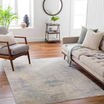 Living room scene with a Razi Avant Garde rug in brown, teal, and gray. Sofa, chair, wood floors, and natural light. Roomscene-Rectangle