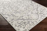 Close-up of the Rockeagle Area Rug. Beige and gray rug with a traditional, floral-inspired pattern on dark wood floors. Corner