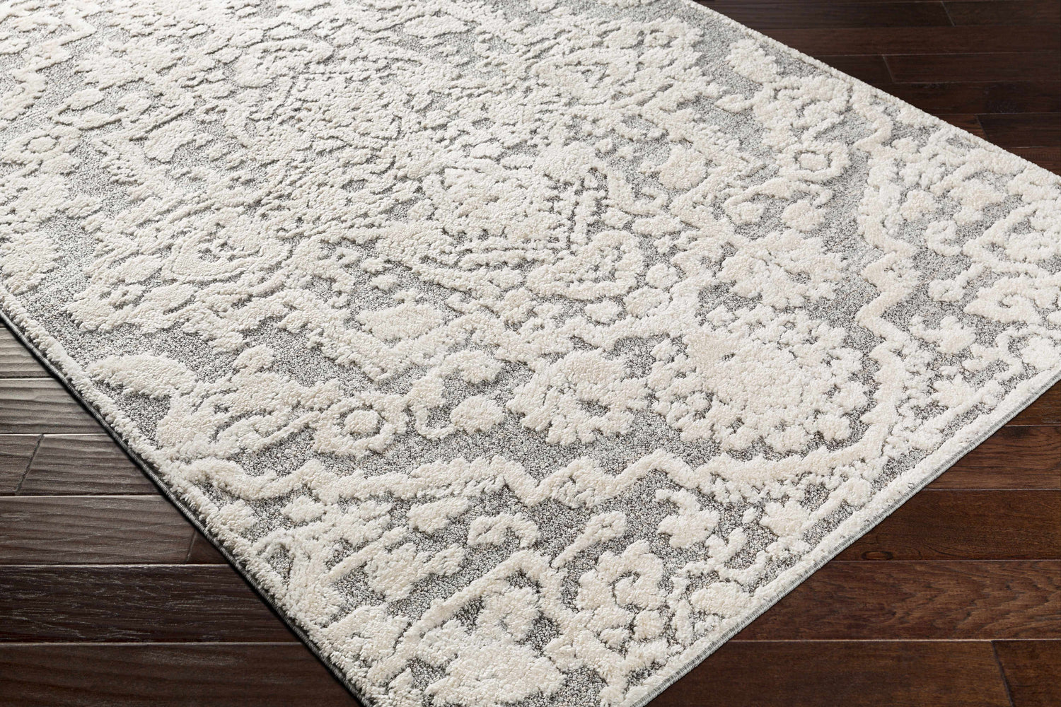 Close-up of the Rockeagle Area Rug. Beige and gray rug with a traditional, floral-inspired pattern on dark wood floors. Corner