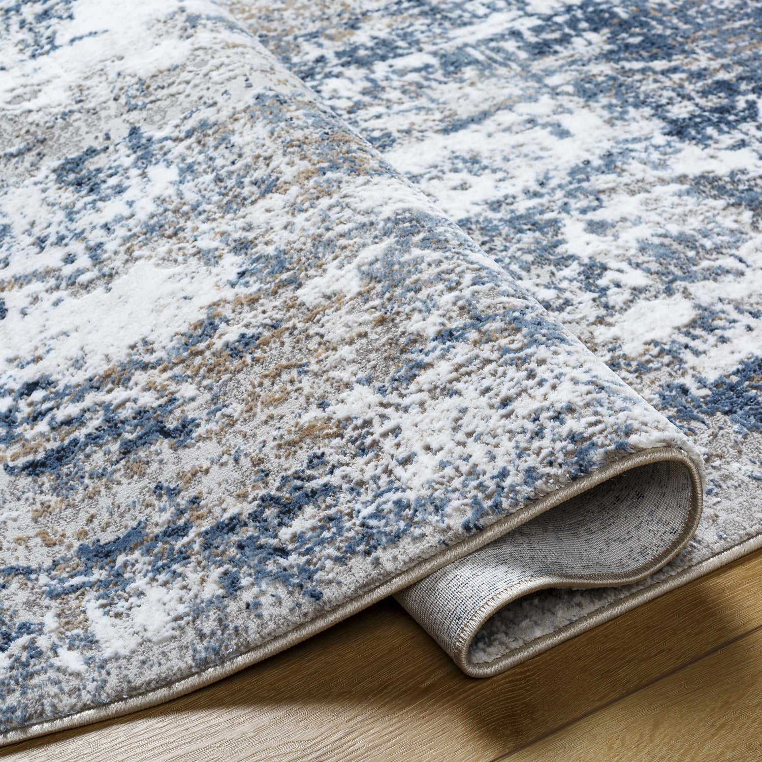 Close-up of the Ord Area Rug showing its abstract pattern in denim, ivory, and gray hues. Machine-woven polyester texture. Fold