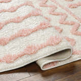 Close-up of the Darva Pink Plush Area Carpet showing its plush texture and pink wavy design on a cream background. Fold