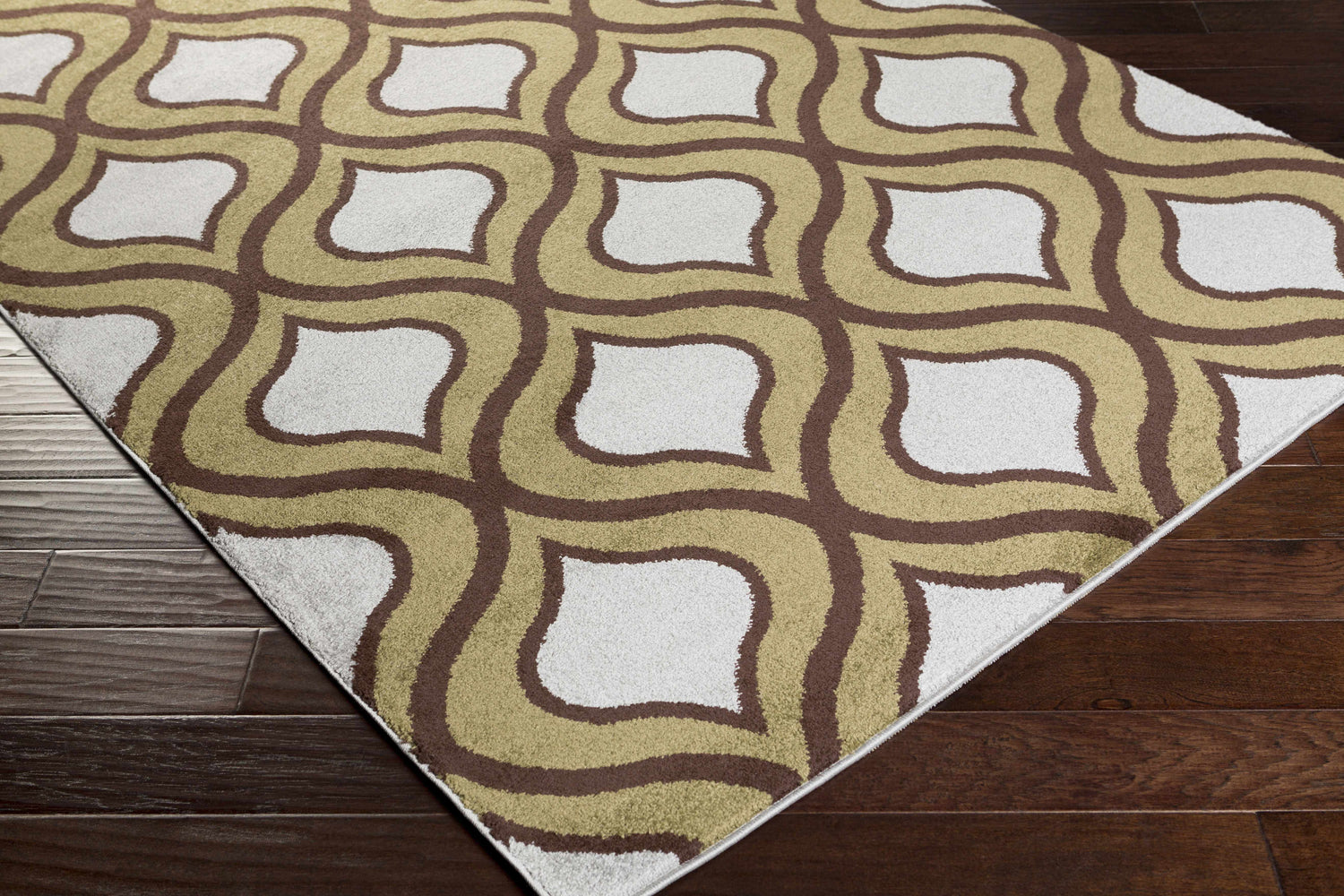 Close-up of the Reeders Area Rug, showcasing its retro olive, brown, and white geometric pattern on dark wood floors. Corner