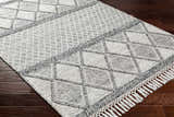 Close-up of the Rehn Area Rug: dark gray and light gray diamond pattern, hand woven with fringe detail on dark wood floor. Corner
