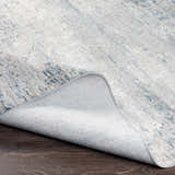 Close-up of the Rendlesham Luxe Rug showing its cream, gray, and teal abstract design and woven texture. Fold