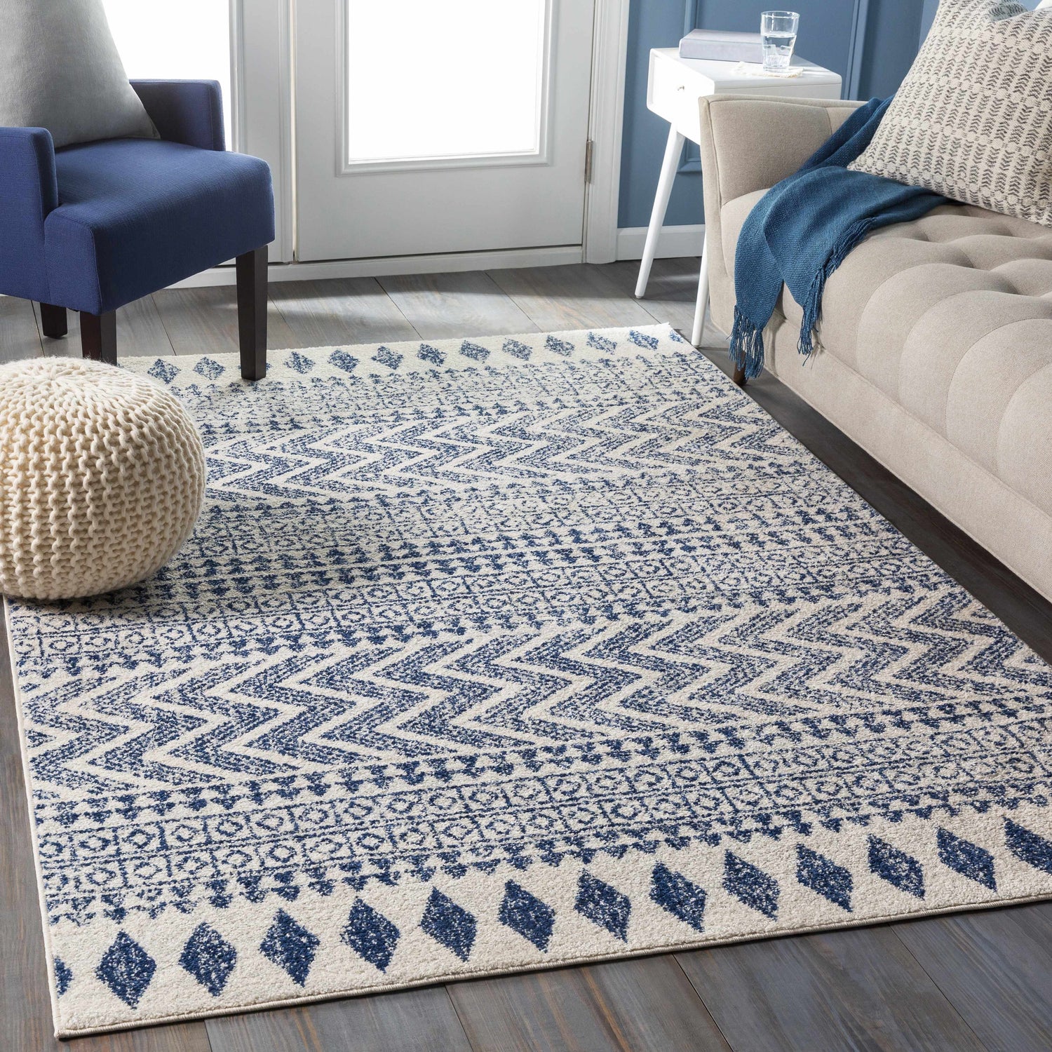 Living room scene with a Renick Area Rug, featuring a blue geometric pattern, beige sofa, and blue armchair. Roomscene-Rectangle