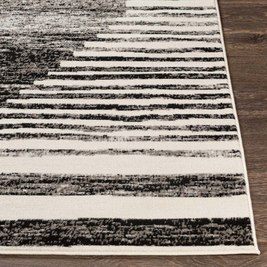 Close up of Resolven Area Rug featuring a black, charcoal, and light gray striped pattern on a wood floor. Front