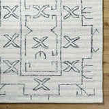 Close-up of the hand-tufted Rider Area Rug. Light silver wool rug with an off-white base and geometric X pattern. Corner