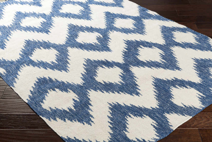 Close-up of the Oradell Blue Ikat Wool Rug with a cream and navy geometric pattern on dark wood floors. Corner