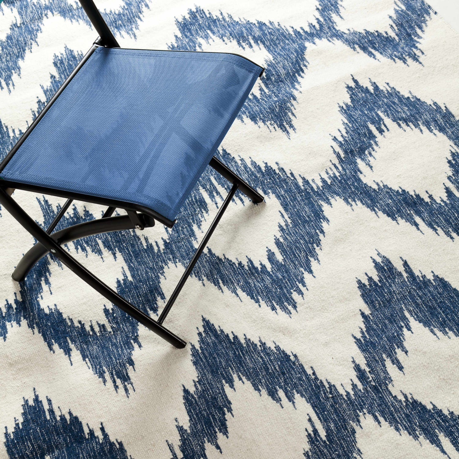 Close up of the Oradell Blue Ikat Wool Rug with a blue folding chair. Cream and navy contemporary rug pattern. Styleshot