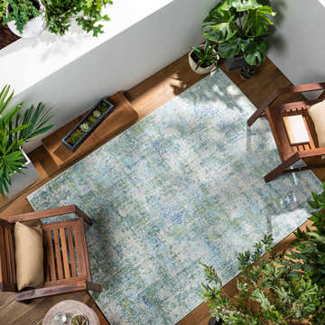 Coastal sunroom with the Riegelwood Area Rug, wooden chairs, and lush green plants. Roomscene-Rectangle