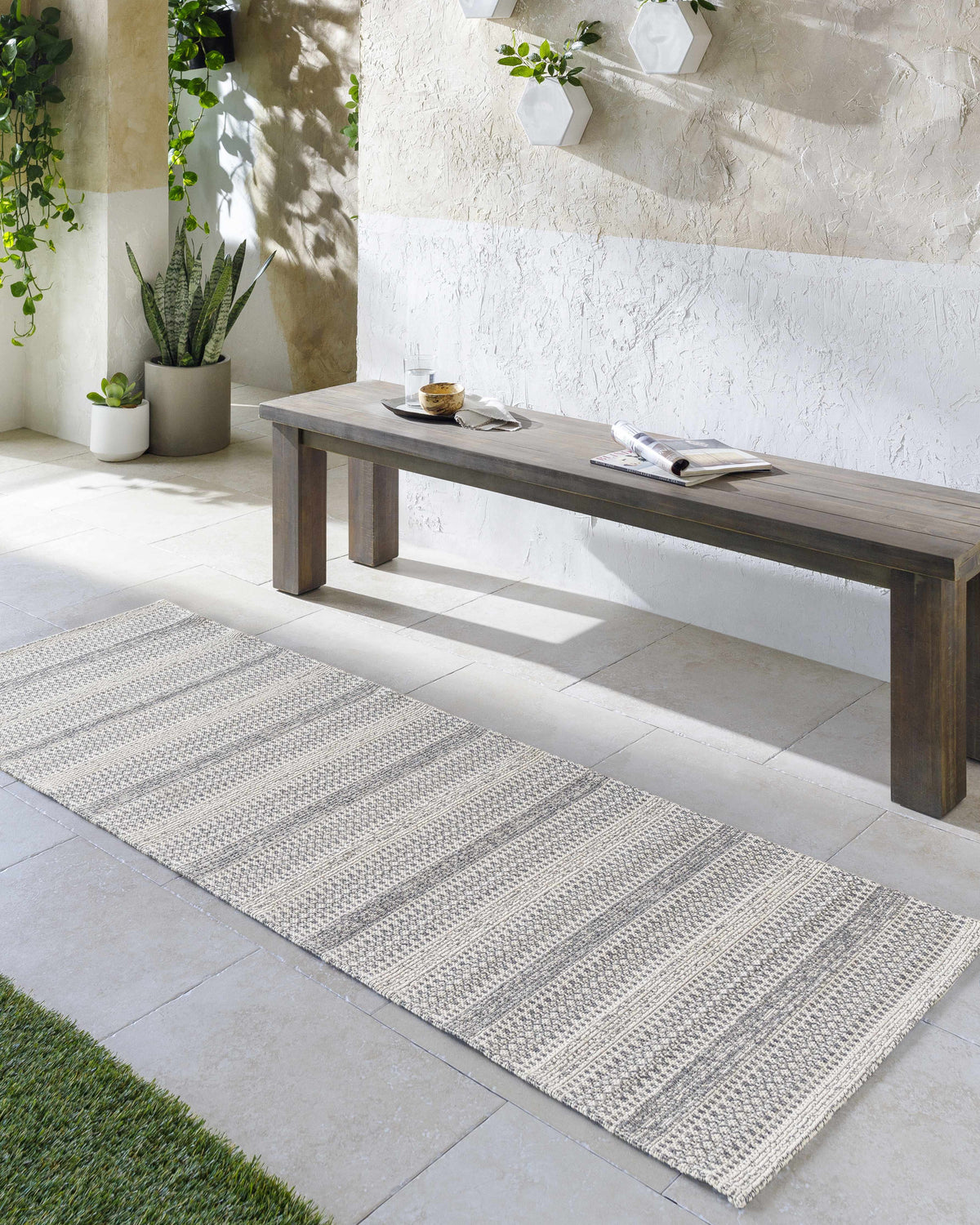 Outdoor patio scene with a charcoal and ivory Ringtown Washable Area Rug, bench, plants, and neutral tones. Roomscene-Runner