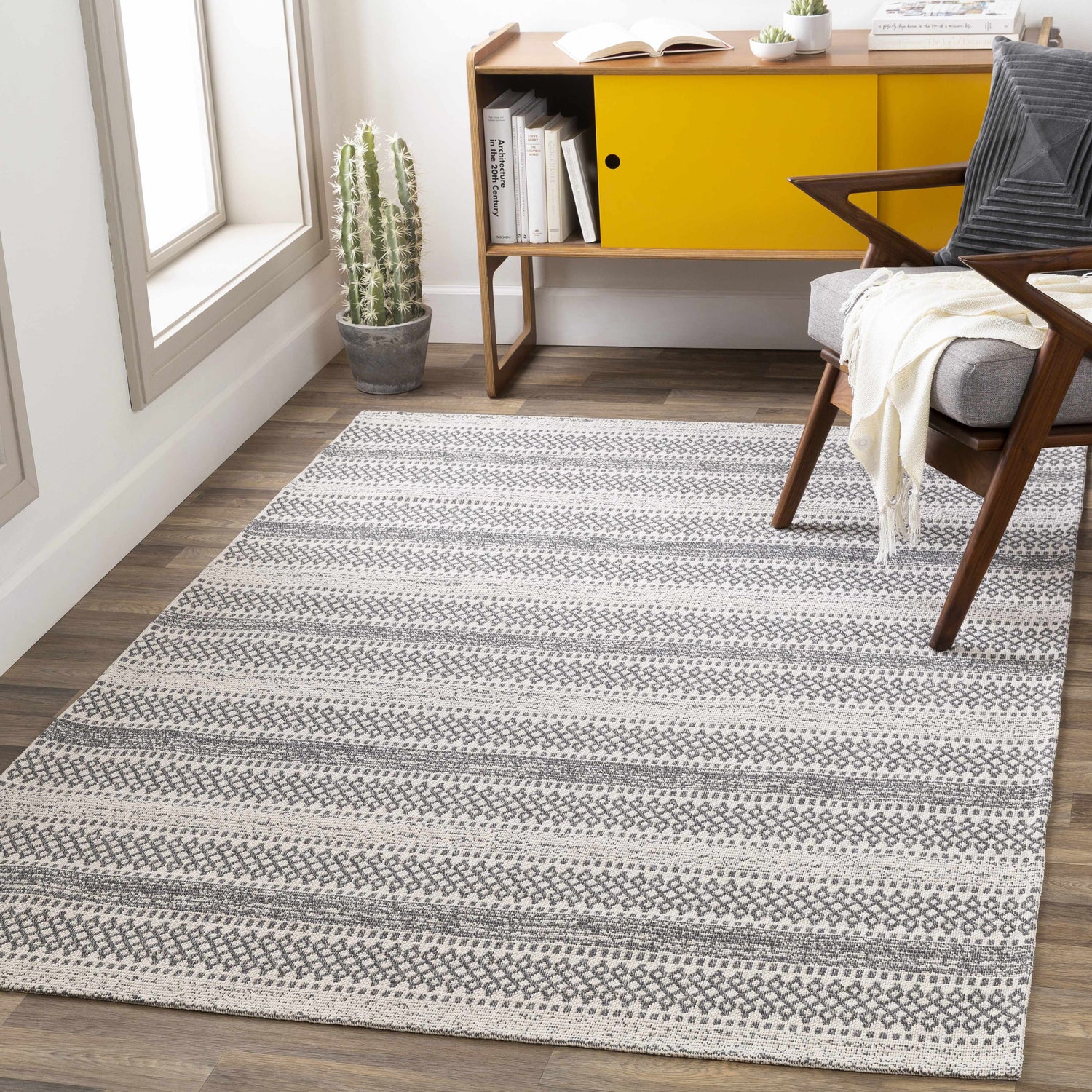 Living room scene with a charcoal and ivory Ringtown Washable Area Rug, wood floors, yellow cabinet, and mid-century chair. Roomscene-Rectangle
