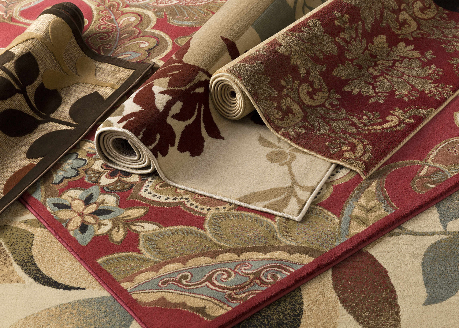 Close-up of rolled Ober Fall Leaves Rugs, showing floral and leaf patterns in red, brown, and beige tones. Styleshot