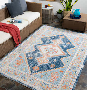 Outdoor patio scene with the Orangeville Area Rug in brick red, cream, denim, and navy. Wicker furniture and slate tile flooring. Roomscene-Rectangle