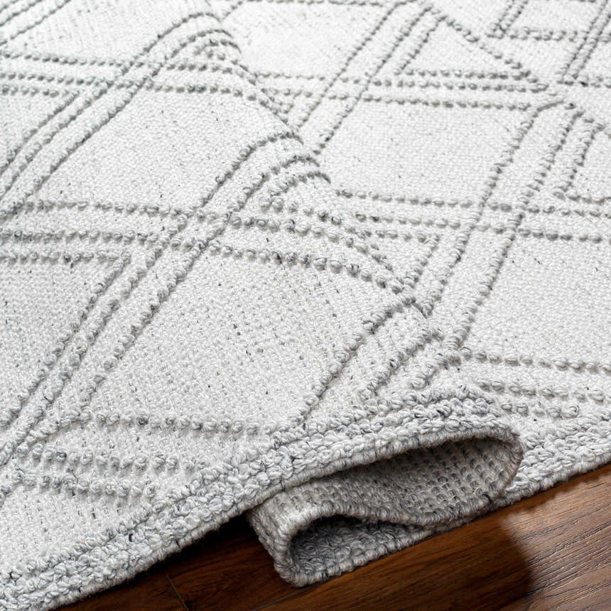 Close-up of the hand woven Rena Area Rug. Arctic stone, gray tones, geometric pattern, and textured design. Fold