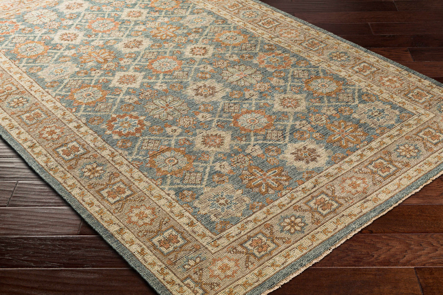 Close-up of Rockton Area Rug on dark wood floor. Traditional floral pattern in dusty sage, light beige, and brown tones. Corner