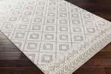 Close-up of the Romeoville Area Rug, a machine-woven rug with a gray and white geometric pattern on a dark wood floor. Corner