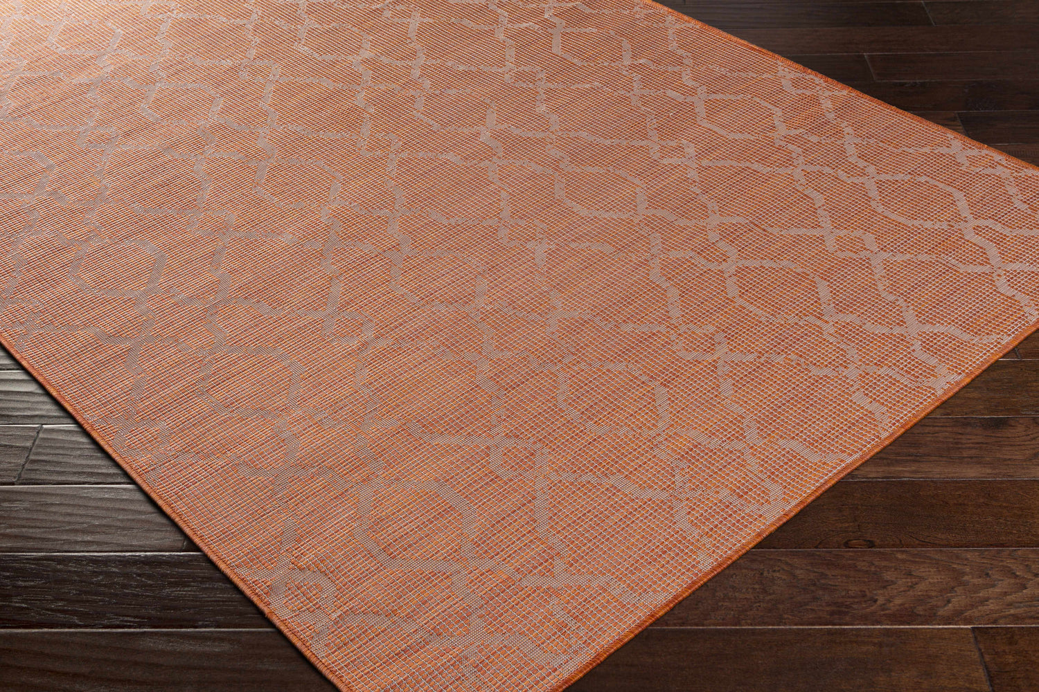Close-up of the burnt orange Rowde Flatweave Area Carpet showing geometric design and woven texture on dark wood floor. Corner