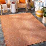 Burnt orange Rowde Flatweave Area Carpet on a patio with wicker chairs and stone tile flooring. Roomscene-Rectangle