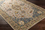 Close-up of the hand-tufted Rozel Area Rug. Traditional oriental rug design in light beige, brown, teal, and mustard on dark wood floor. Corner
