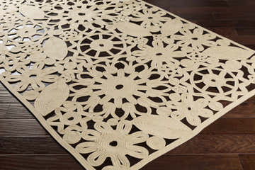 Close up of beige Ruxton Area Carpet showing floral and leaf pattern on dark wood floor. Hand woven texture. Corner