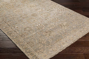 Close-up of the hand-knotted Ravenshead Area Rug. Dusty sage, light beige, and taupe oriental rug on dark wood floor. Corner