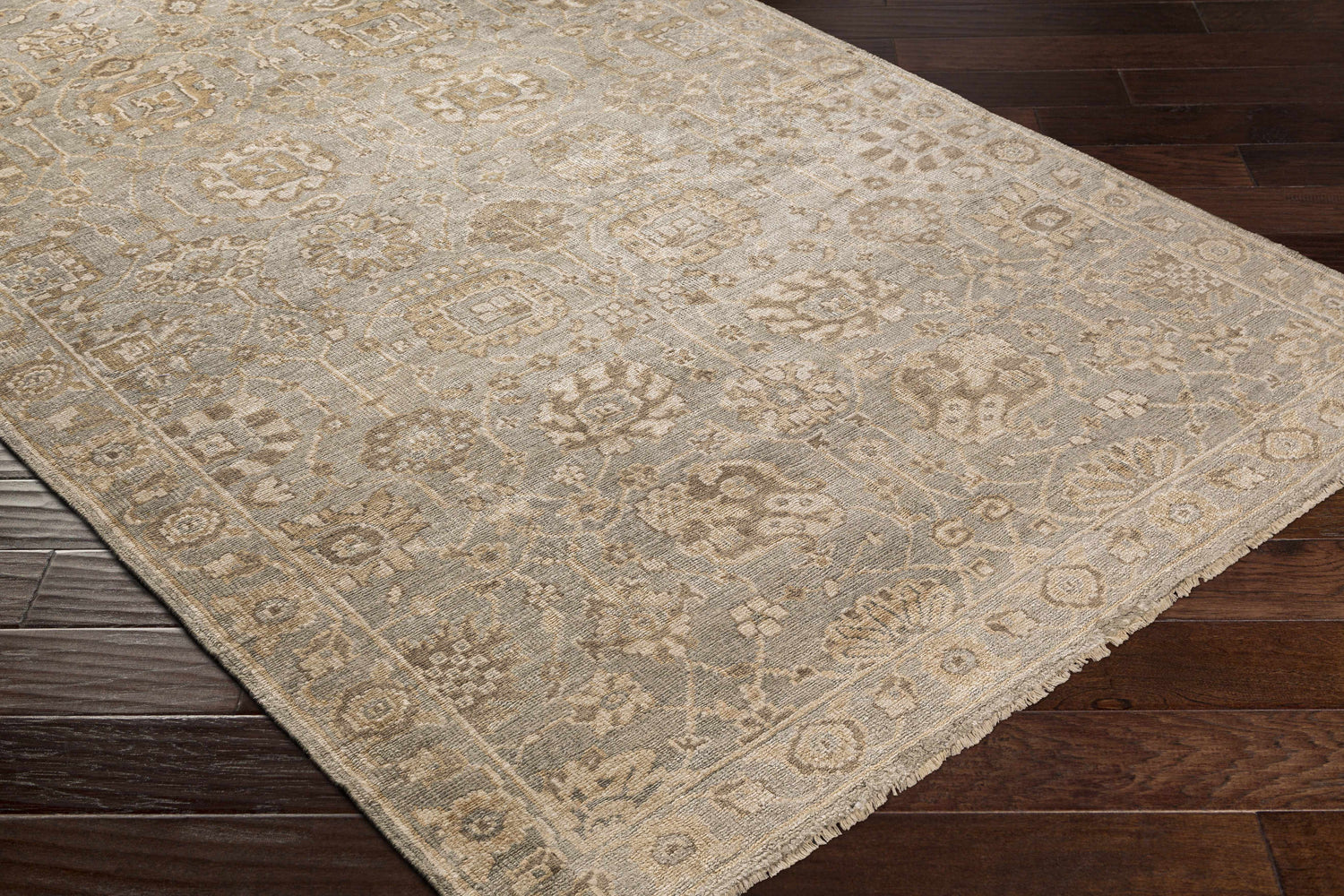 Close-up of the hand-knotted Ravenshead Area Rug. Dusty sage, light beige, and taupe oriental rug on dark wood floor. Corner