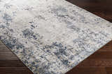 Close-up of the Ryhill Textured Luxe Area Rug. Charcoal, light beige, and gray abstract pattern on dark wood floors. Corner