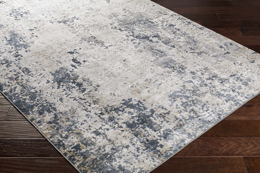 Close-up of the Ryhill Textured Luxe Area Rug. Charcoal, light beige, and gray abstract pattern on dark wood floors. Corner